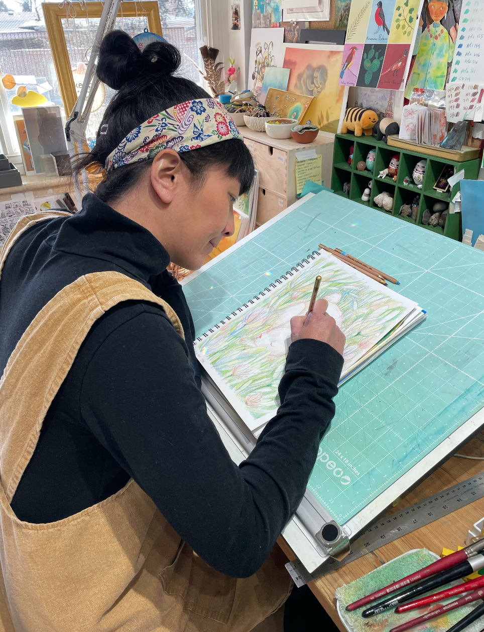 Pictured: Saki Tanaka drawing in her sketchbook at her table in her studio.